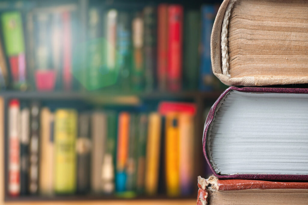Photo of Books on desk with full bookshelf in background